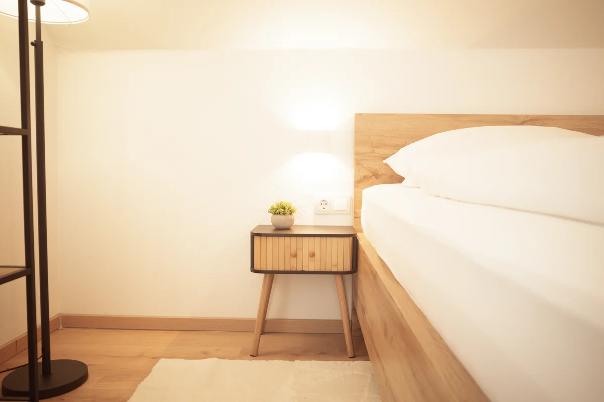 Holznachttisch, Leselampe und weiße Bettwäsche im Doppelzimmer mit Balkon
