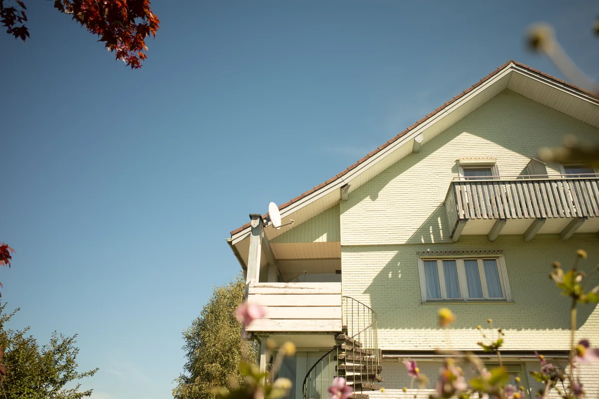 Hausfassade mit Balkonen, blauem Himmel und Blumen im Vordergrund