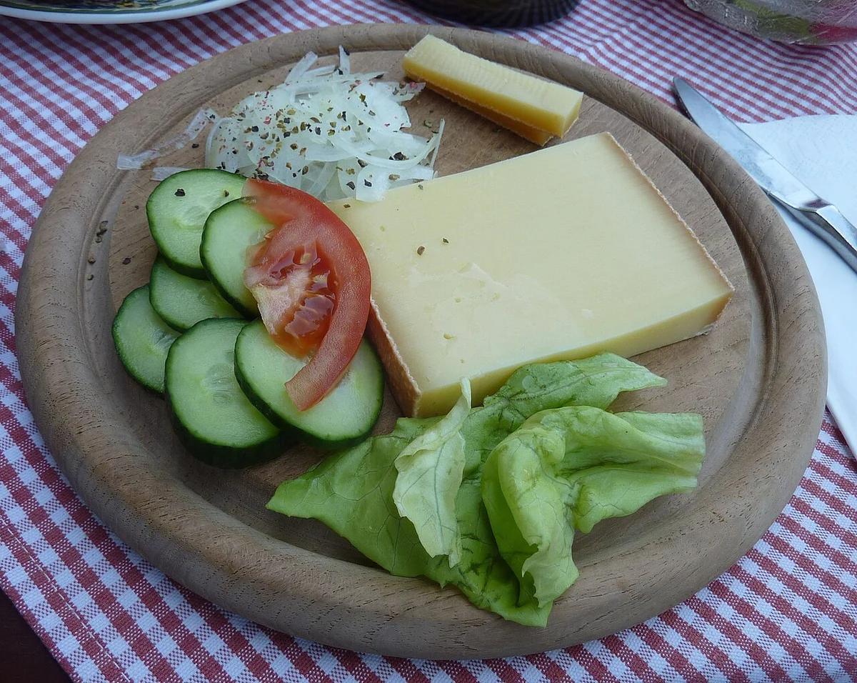 Allgäuer Bergkäse mit Salat und Gemüse auf einem rustikalen Holzteller – regionale Käsespezialität