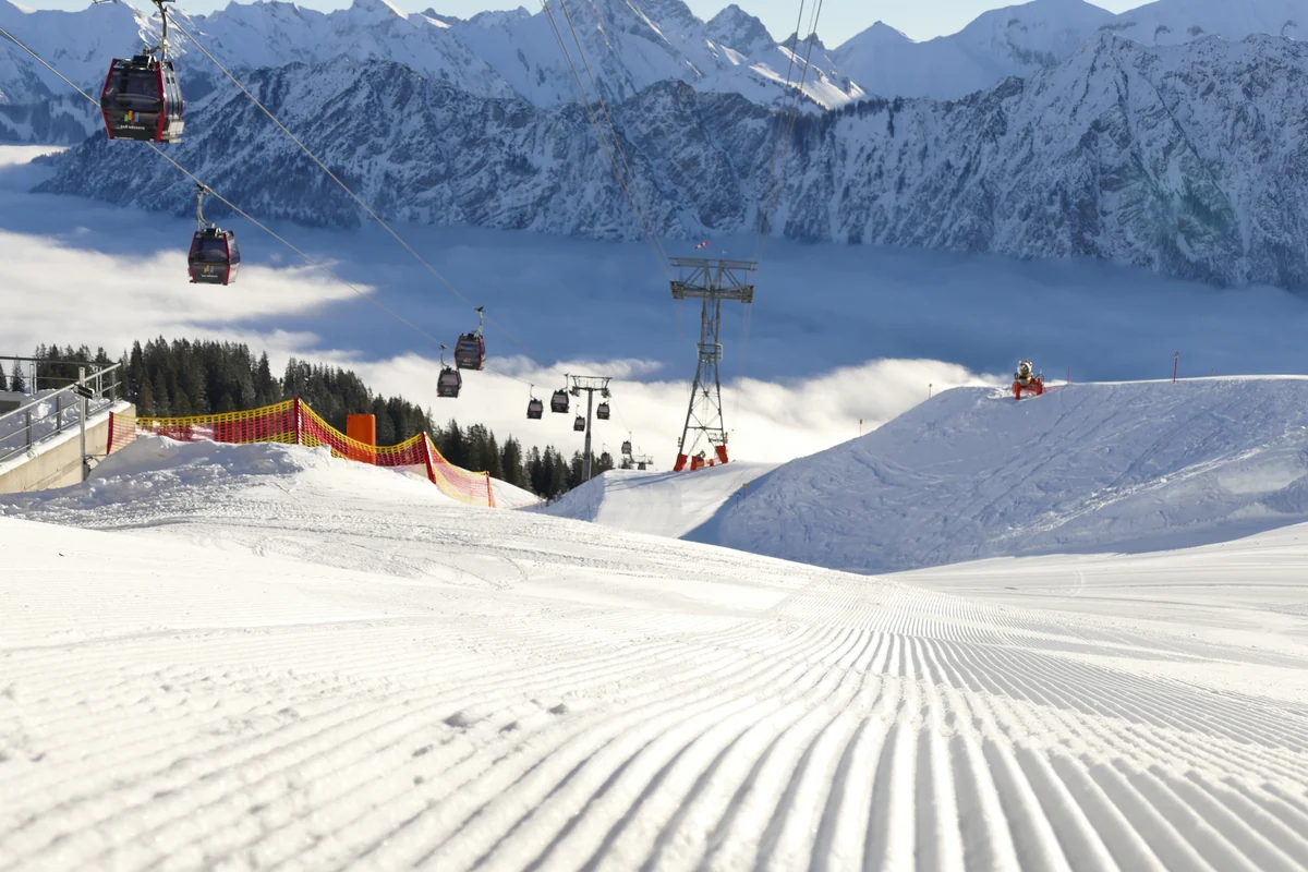 Frisch präparierte Skipiste mit Gondeln der Fellhornbahn und verschneitem Bergpanorama bei Oberstdorf